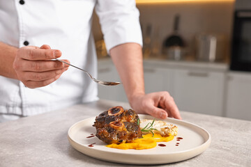 Professional chef adding sauce to delicious dish at table indoors, closeup