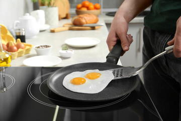 Man taking fried eggs from frying pan in kitchen, closeup