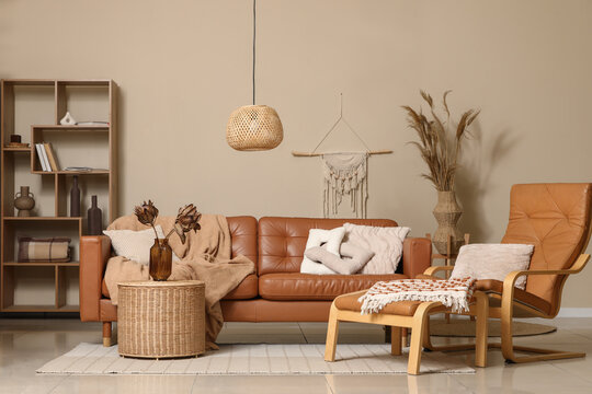 Comfortable sofa, armchair with footrest and dried flowers in vase on basket in interior of living room