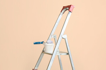 Maintenance ladder with paint and roller near beige wall