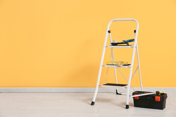 Maintenance ladder with instruments and paint tools near yellow wall