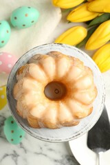 Delicious bundt cake, Easter eggs and tulips on white marble table, flat lay