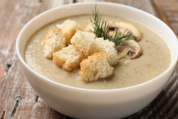 Delicious mushroom cream soup with croutons and dill on wooden table, closeup