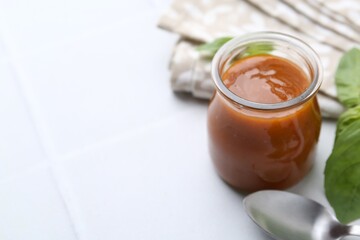 Tasty curry sauce in glass jar and basil on white tiled table, closeup. Space for text