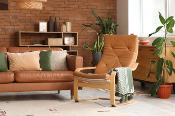 Interior of living room with leather sofa, armchair, houseplants and shelving unit near window
