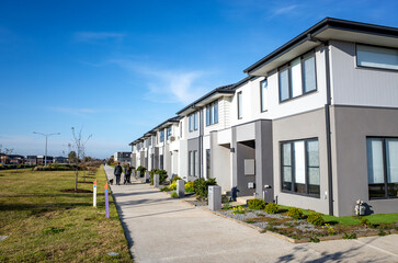 A row of contemporary Australian townhouses. Modern multi-unit dwellings along a concrete pathway with small front gardens and an open green community space.