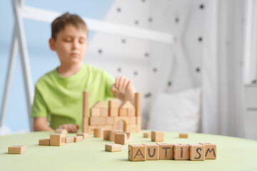 Cubes with word AUTISM on table against little boy at home, closeup