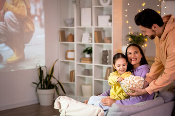 Family eating popcorn while watching movie at home