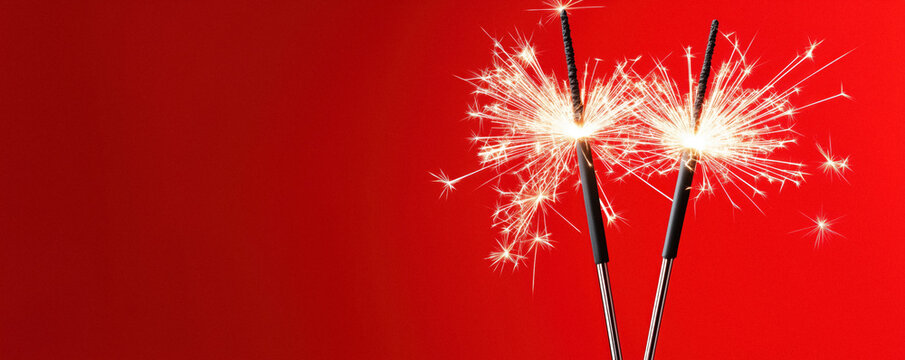 Close-up of two sparklers lit against a red background. - Powered by Adobe