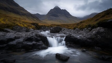 Obraz premium Panoramic view of waterfall at fairy pools on a grey autumn day. Water flowing over rocks with mountains in the background.