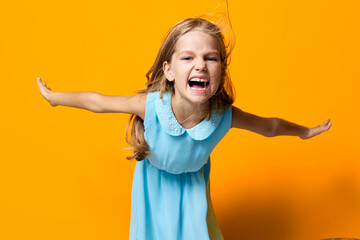 Joyful little girl in a blue dress jumping with excitement against a vibrant orange background