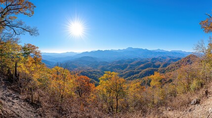A breathtaking panoramic view of colorful autumn foliage under a bright sun, showcasing layered mountains and clear blue skies.