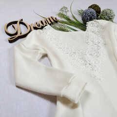 Elegant white long-sleeve top with delicate lace detailing at the neckline. Perfect for a dreamy, romantic look. Paired with dried flowers and a "Dream" sign for a whimsical vibe.