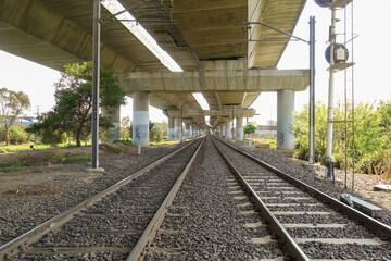 Train tracks or railroad running beneath an elevated concrete highway or overpass bridge with...