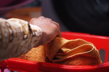 Hand sorting clean towels into a red laundry basket indoors