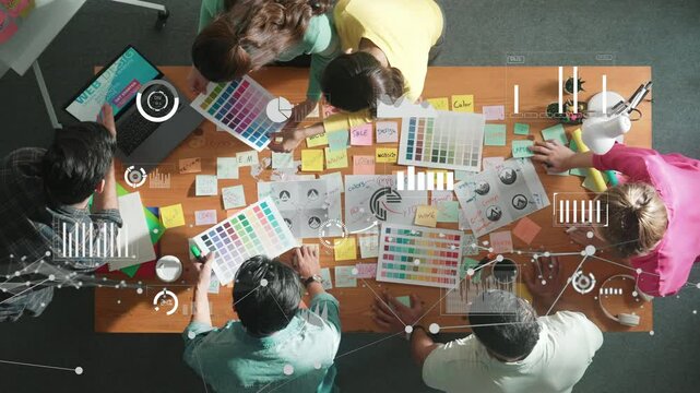 Top down view of business team with casual outfit looking laptop screen and sharing idea. Aerial view of manager works and checking color palette at table with statistic graph holographic. Symposium.