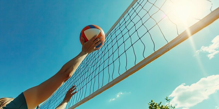 Volleyball player spiking the ball towards the net, blue sky background