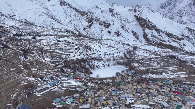 Aerial drone shot showcasing the serene beauty of Nako Lake, completely frozen and encircled by a thick blanket of snow in the winter landscape.