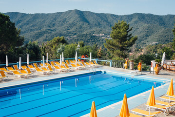 Piscine dans un camping en Italie. Grande piscine bleue, parasols et transats jaunes, paysage de montagne. Personne. Absence de clients. Pas de touriste. Vacances en Italie