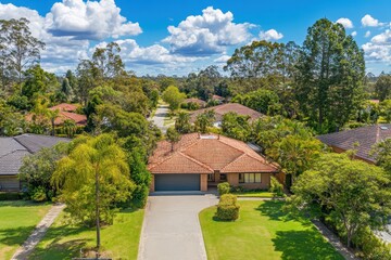 An aerial view showcases a suburban home, lawn, trees, and blue sky. Showcase real estate or suburban living with this bright, sunny shot.