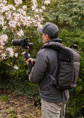 Man with professional camera on stabilizer records video blossoming trees in city park. Creative process nature photography. Suitable for photography, videography, technology, content creation.