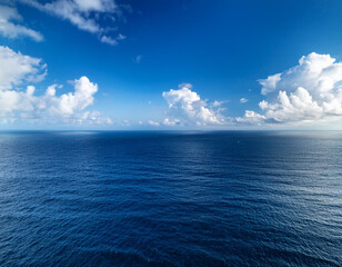 Obraz premium A deep blue ocean horizon meeting a vast sky with rolling white clouds forming light shadows over the sea.