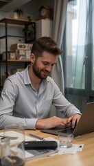 Fototapeta premium Young man smiling while working on a laptop in a cozy office 