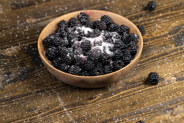 ripe black blackberries in a wooden bowl sprinkled with sugar