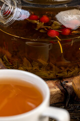 red rosehip fruits and hot green tea in a transparent teapot