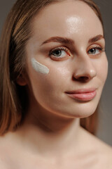 Naklejka premium Woman applying skincare cream on her cheek in a softly lit indoor space during daytime