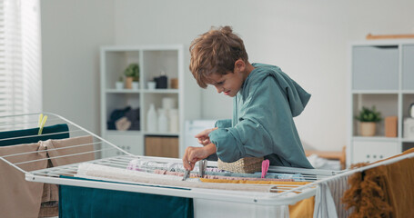 The boy helps his family by clipping clean laundry on the drying rack in the bathroom. He enjoys...