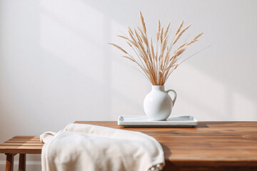 Simple still life featuring a white vase filled with dried wheat or grass on a wooden table. Soft natural light and a beige cloth add to the serene and minimalist scene.
