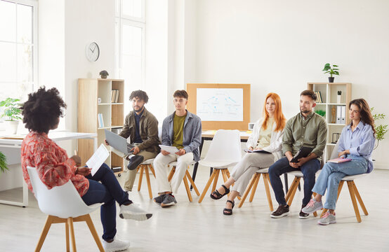 African American businesswoman leading a business meeting or training session in the office setting for a team of professionals. The group of people focuses on communication and teamwork.
