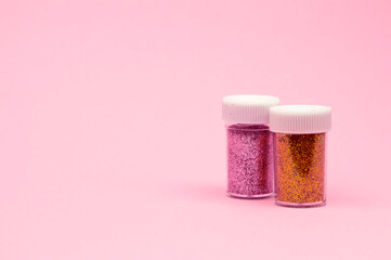 A close-up top view of tiny colorful sequins in round containers, elegantly scattered on a soft pink backdrop.