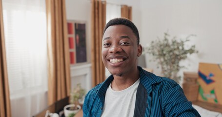 Obraz premium Smiling guy records vlog, video on social media, talking through camera with family, man shows new apartment, cardboard boxes with packed things, tells impressions