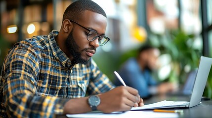 A man with glasses writing in a notebook at desk