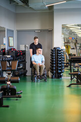 Disabled athlete in wheelchair escorted to training gym workout by attentive personal coach....