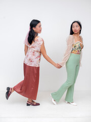 Two Filipino women holding hands as one leads the other, showing playful expressions and connection in floral fashion and pastel outfits.