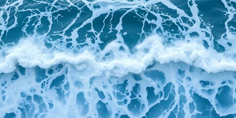Naklejka premium Ocean's Rhythmic Embrace: An overhead, dynamic view of the ocean, showcasing the dance of waves and foam in a mesmerizing aquatic ballet. The rich, vivid blues contrast with the frothy whites.