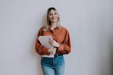 Young woman with papers stands against a neutral background displaying confidence and...