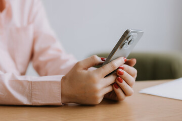 Person using smartphone to check messages while sitting at a wooden table in a bright indoor setting