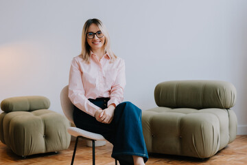 Obraz premium Young woman with glasses sits confidently in a modern living room with stylish furniture