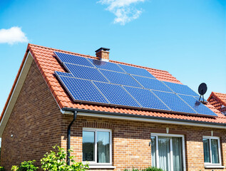 Fototapeta premium Solar panels on red-tiled roof of brick house, realistic style, clear blue sky background. Concept of sustainable energy and modern home architecture. Ai generative
