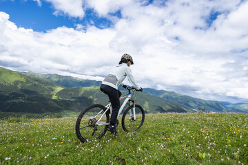 Obraz premium Woman riding mountain bike on flowering grassland mountain trail