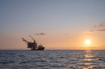 Beautiful image of offshore gas drilling rig as the sun rises in the morning, with service boats approaching.