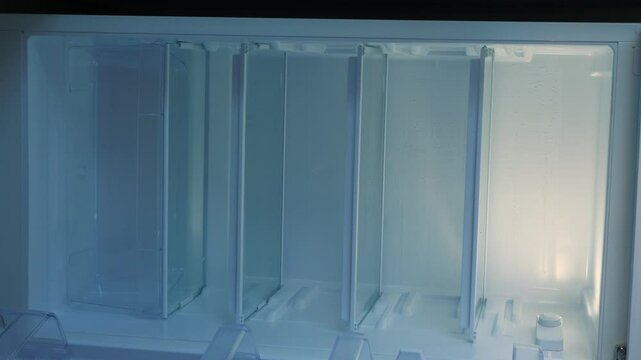 An empty refrigerator with no food, a hand opens and closes the home fridge with empty shelves meant for groceries, vertical video