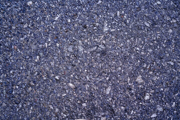 Textured asphalt surface with mix of small stones and gravel, showcasing dark gray color. This durable material is commonly used for roads and pavements, providing sturdy foundation