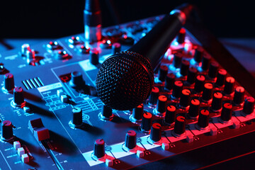 Professional mixing console with microphone on table in neon lights, closeup