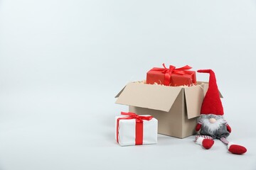 Parcel with gift boxes and decorative dwarf on light background