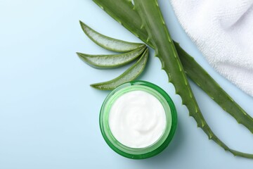 Moisturizing cream with extract of aloe vera, towel and leaves on light blue background, flat lay. Space for text
